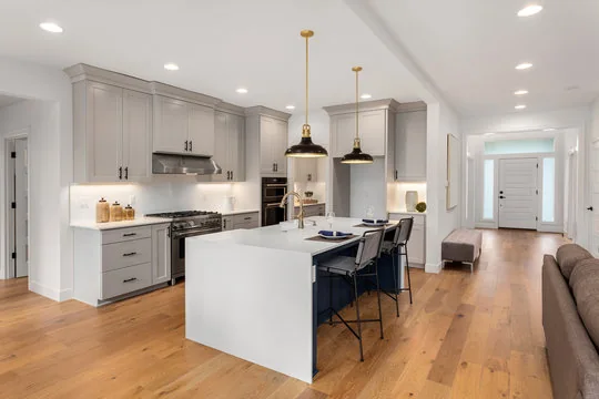 Grey cabinets with white waterfall island and gold pendants in an open-plan home